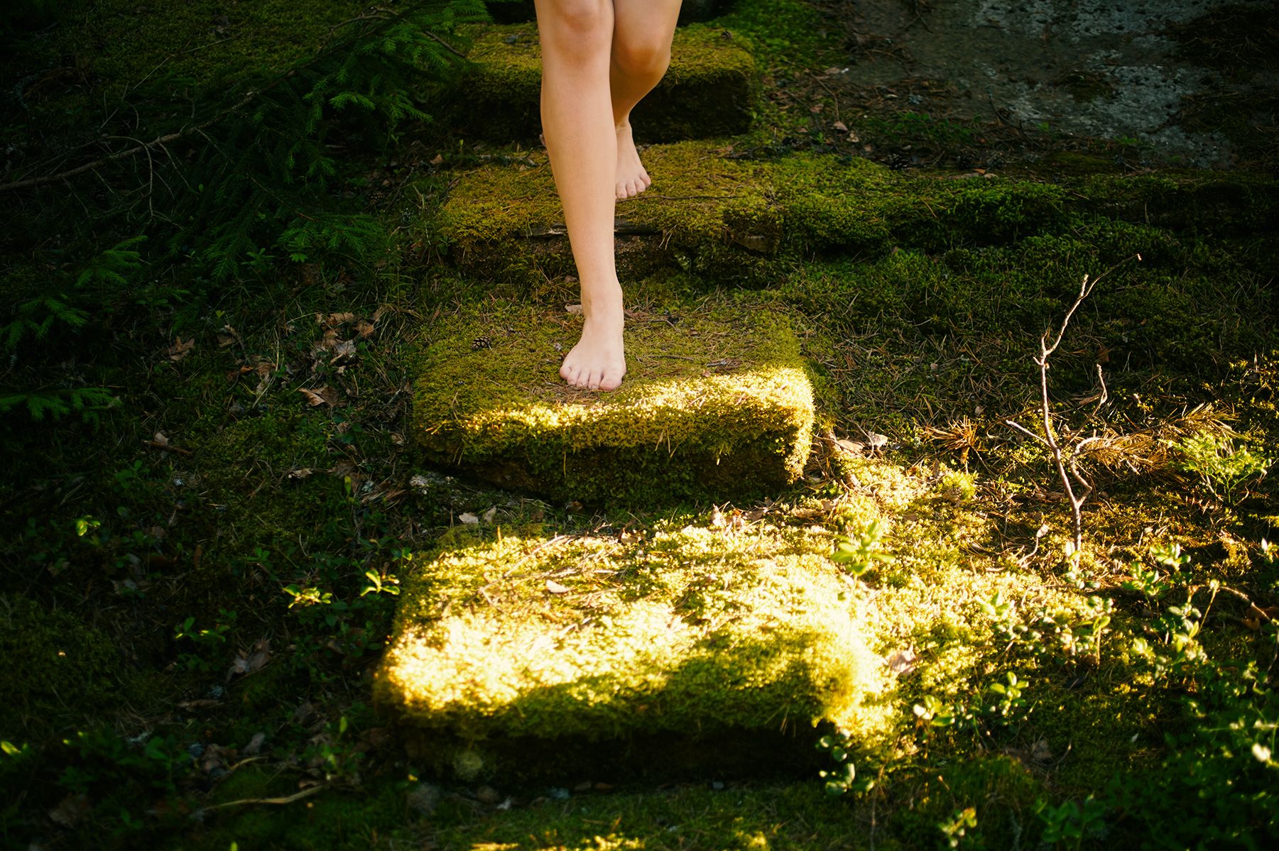 A person's legs stepping on moss-covered stones in the forest.