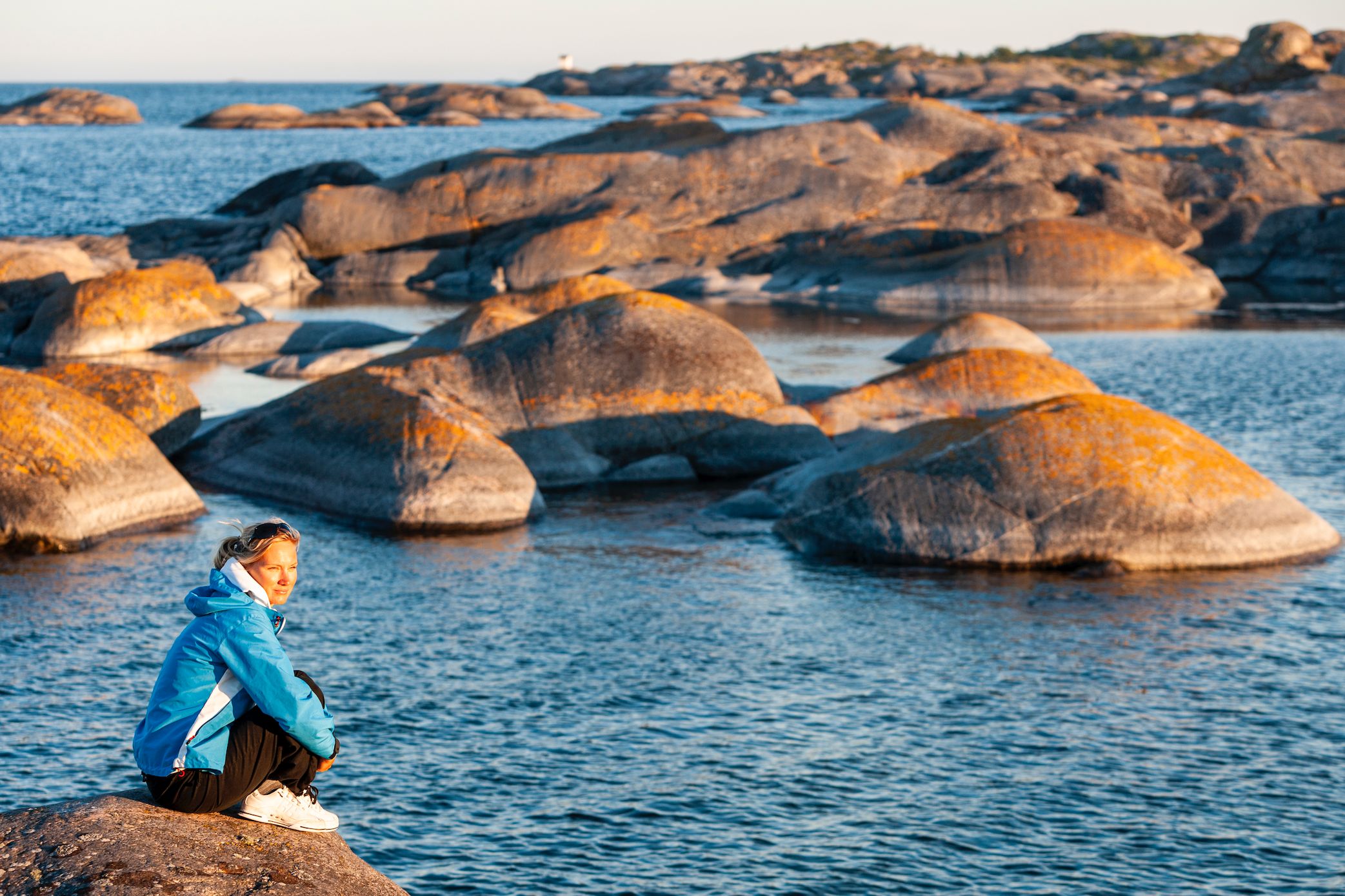En kvinna sitter på en sten vid vattnet