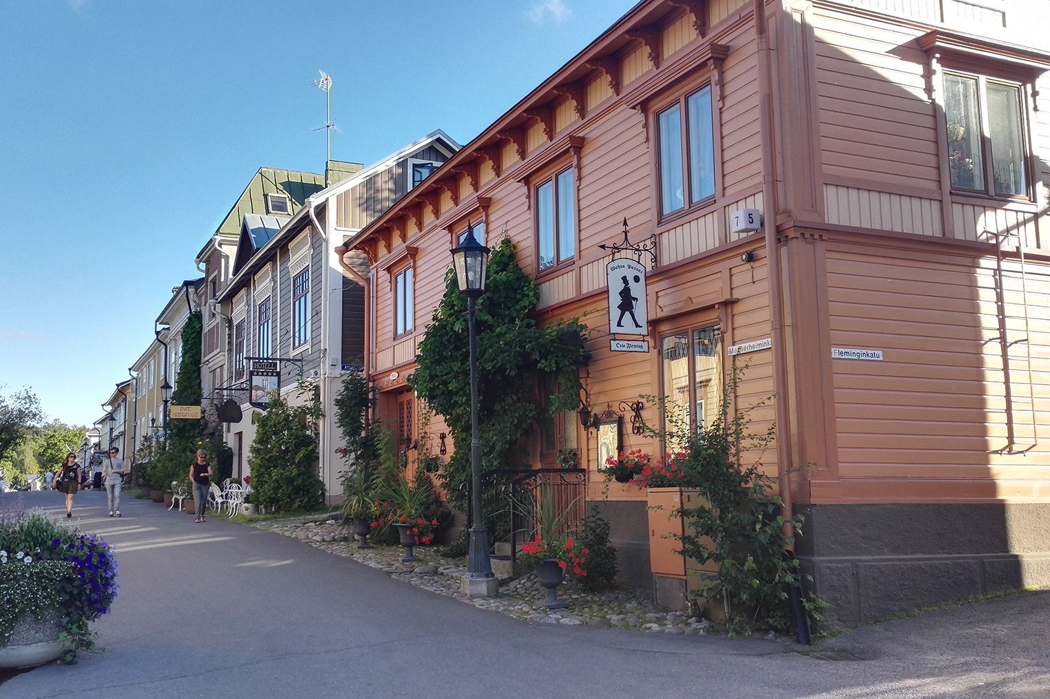 Visitors walk down a street in Naantali, lined with colourful wooden houses.