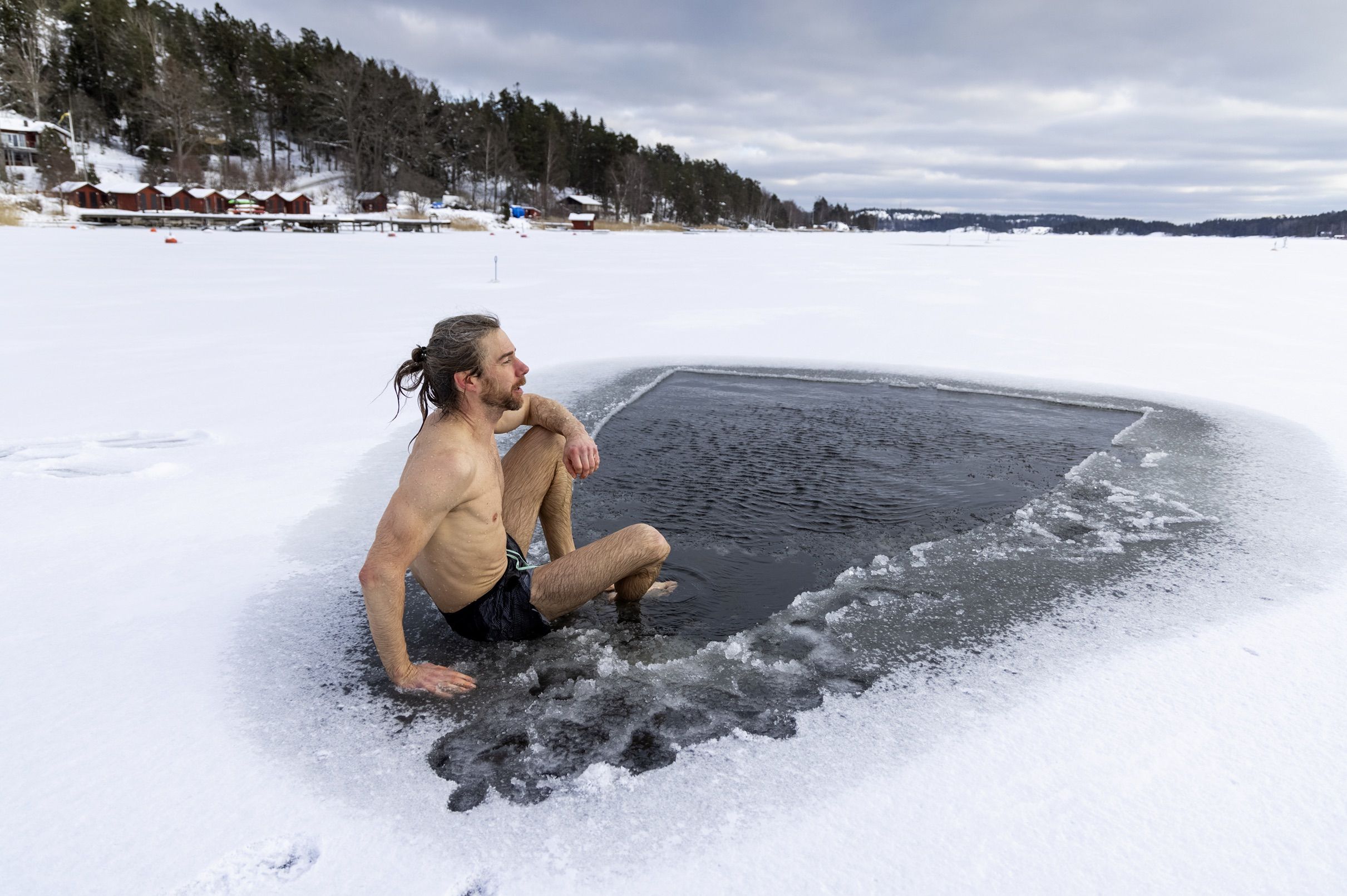 En man sitter avklädd vid en isvak, redo att hoppa i. Foto: Henrik Trygg.
