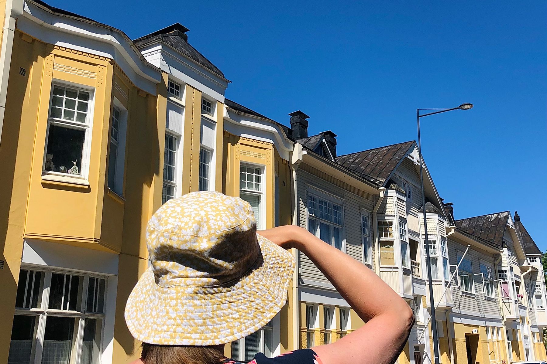 A person in a yellow hat looks at the yellow wooden houses on Piispankatu Street on a bright summer’s day.