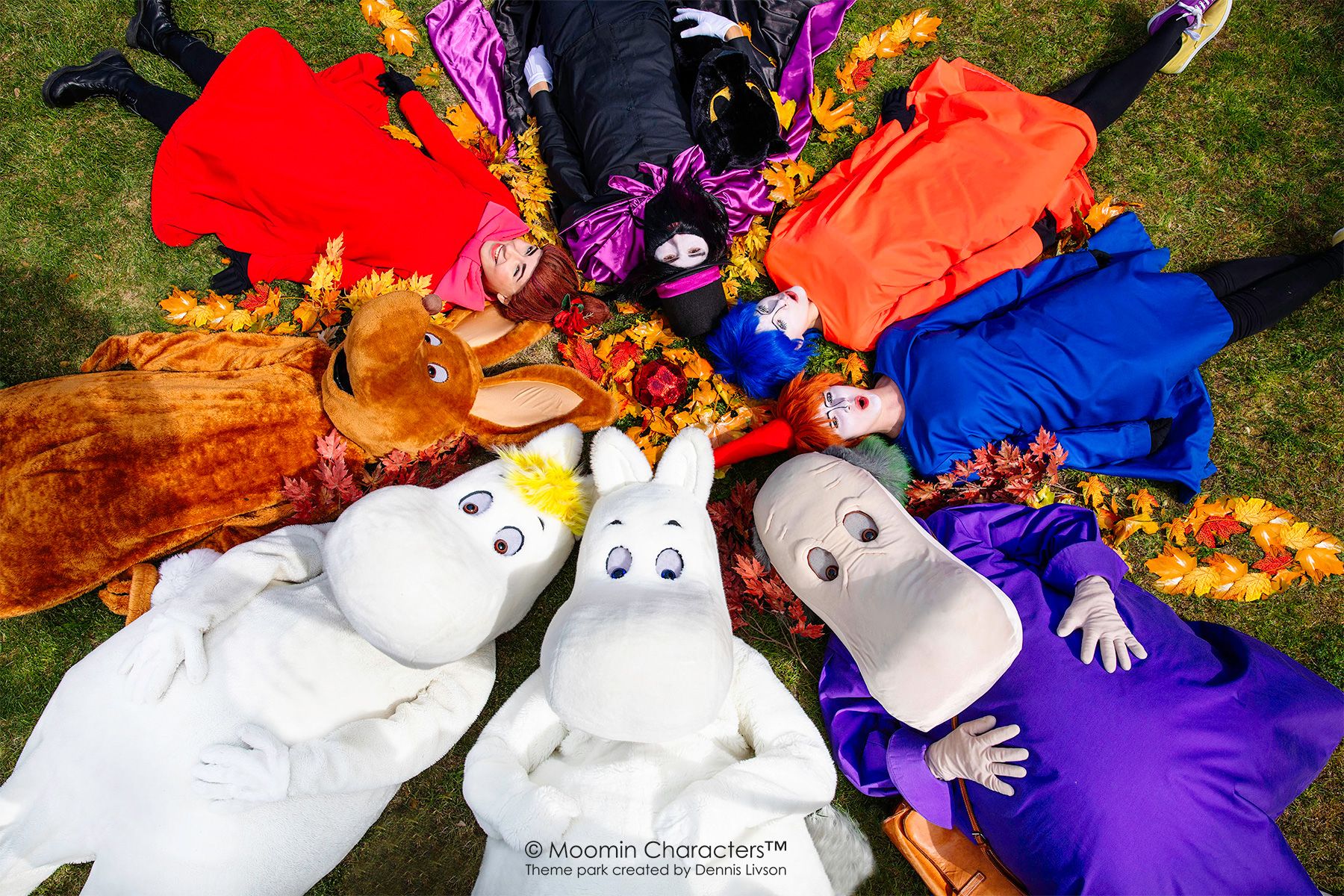 A group of Moomin characters lay on the ground in a circle, their heads meeting together.